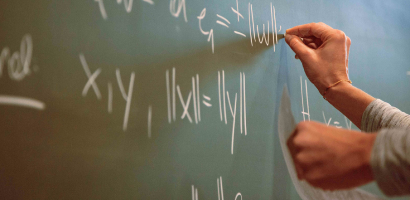 Hands writing maths on a chalkboard